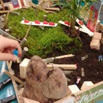 Kinder erstellen ein kleines Dorf in einer Holzkiste mit Pflanzen, Häusern, Autos und Menschen